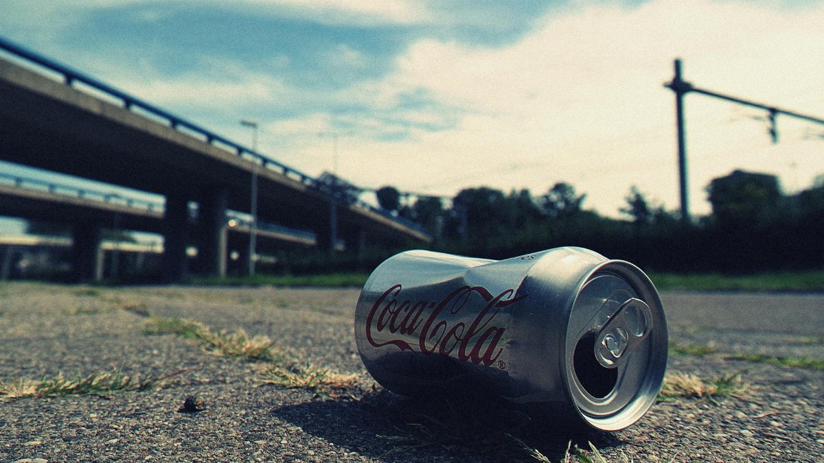 A close-up photo of an empty Coca-Cola can lying on an urban road, symbolizing litter.