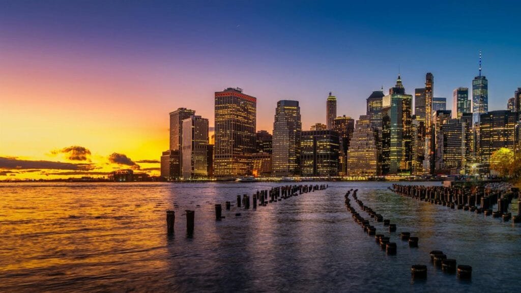 Breathtaking view of New York City's illuminated skyline during a vibrant sunset over the river.
