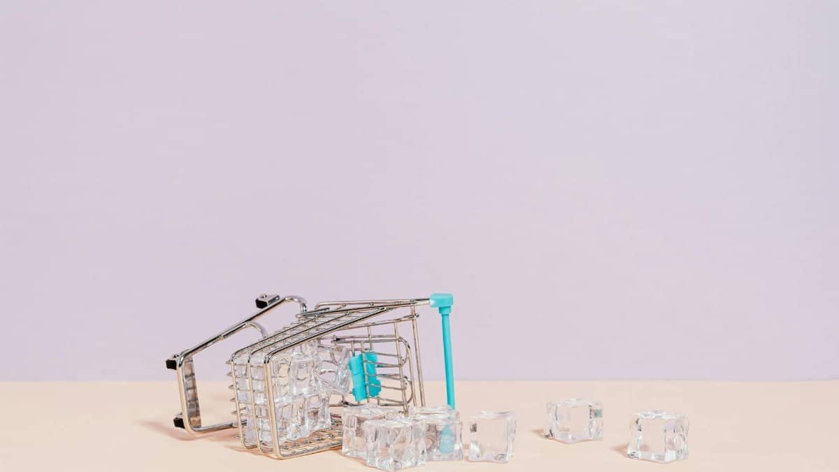 Tipped shopping cart with ice cubes on pastel background, offering creative copy space.