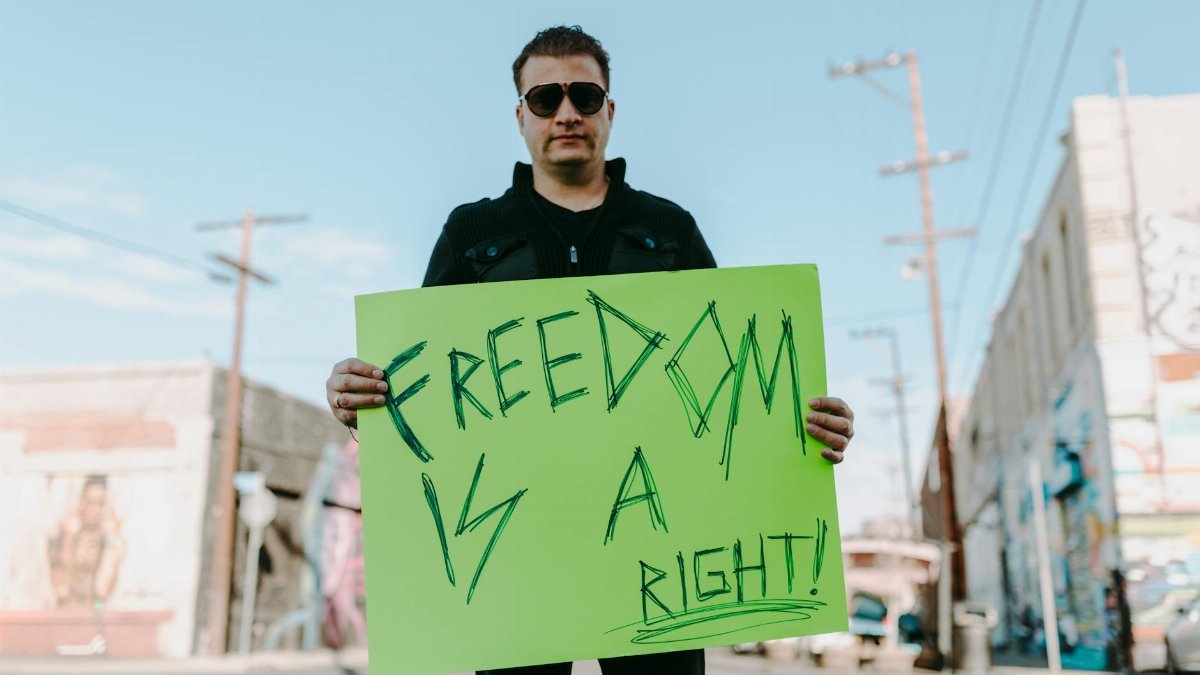 A man holds a bright protest sign stating 'Freedom is a Right!' outdoors.