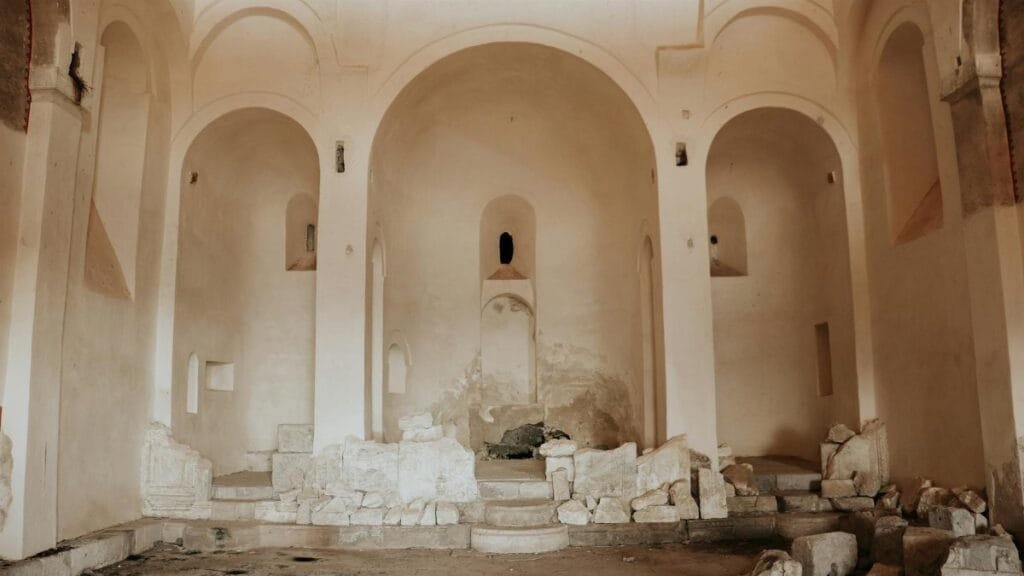 Interior of an abandoned church with crumbling altar and ruins, showcasing historical religious architecture.