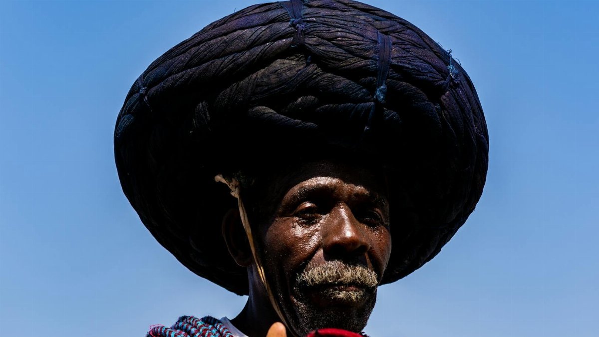 Portrait of an elderly man wearing traditional African clothing under a clear blue sky.