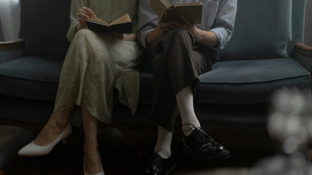 A man and woman sitting on a sofa, reading books together in a cozy indoor setting.