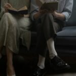 A man and woman sitting on a sofa, reading books together in a cozy indoor setting.