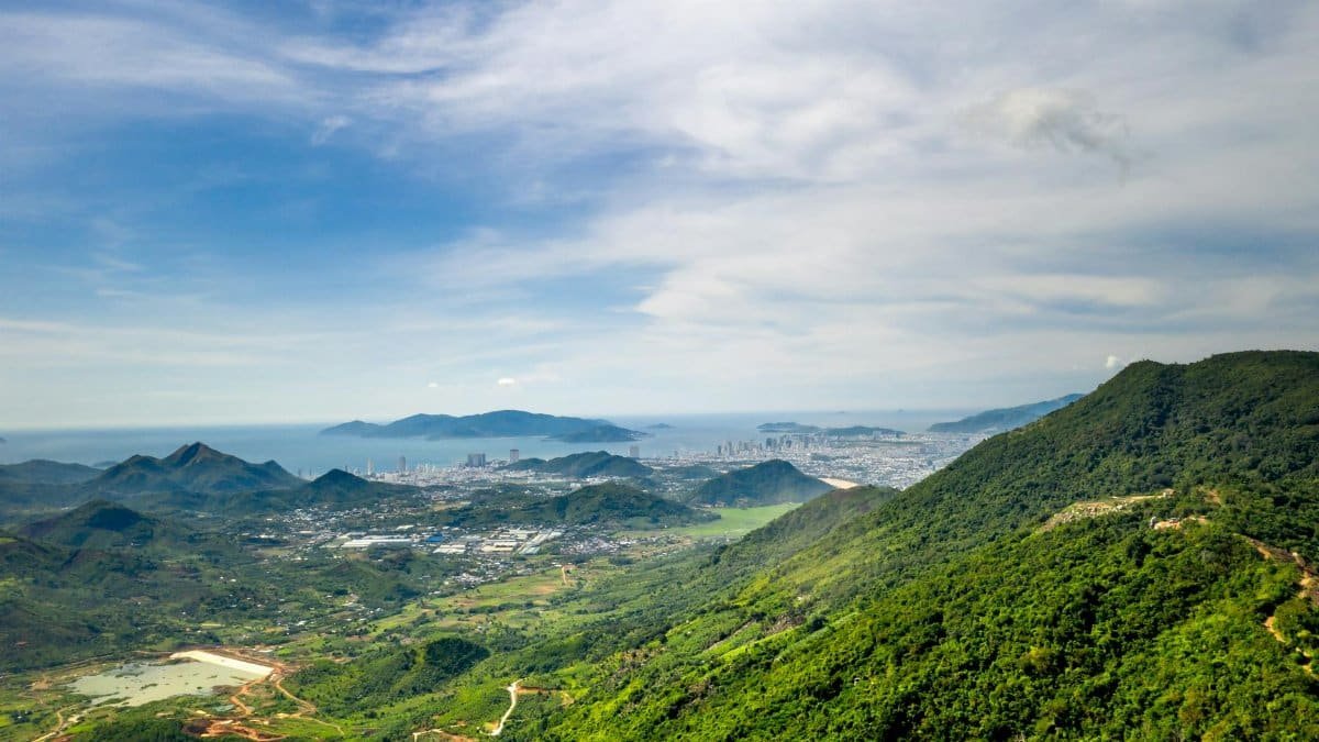 Breathtaking aerial view of a lush green mountain landscape with a coastal city in the background.