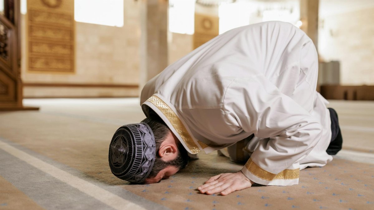 A Muslim man in traditional attire praying inside a mosque, showcasing cultural reverence.
