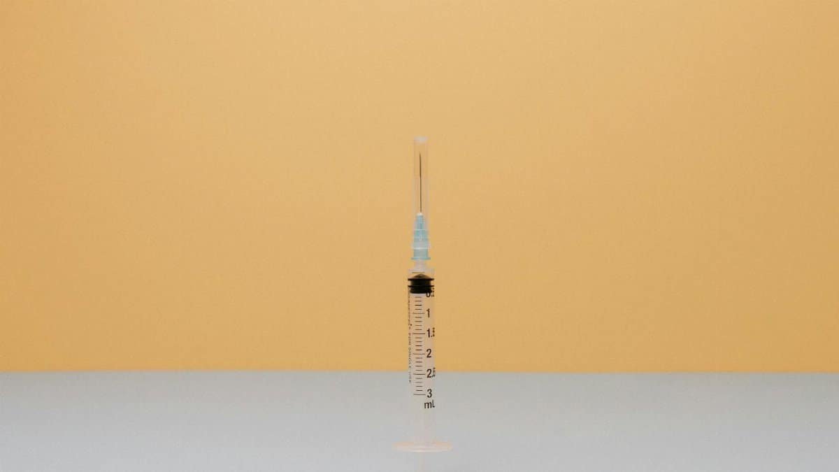 Close-up of a syringe on a pastel surface with a warm backdrop.