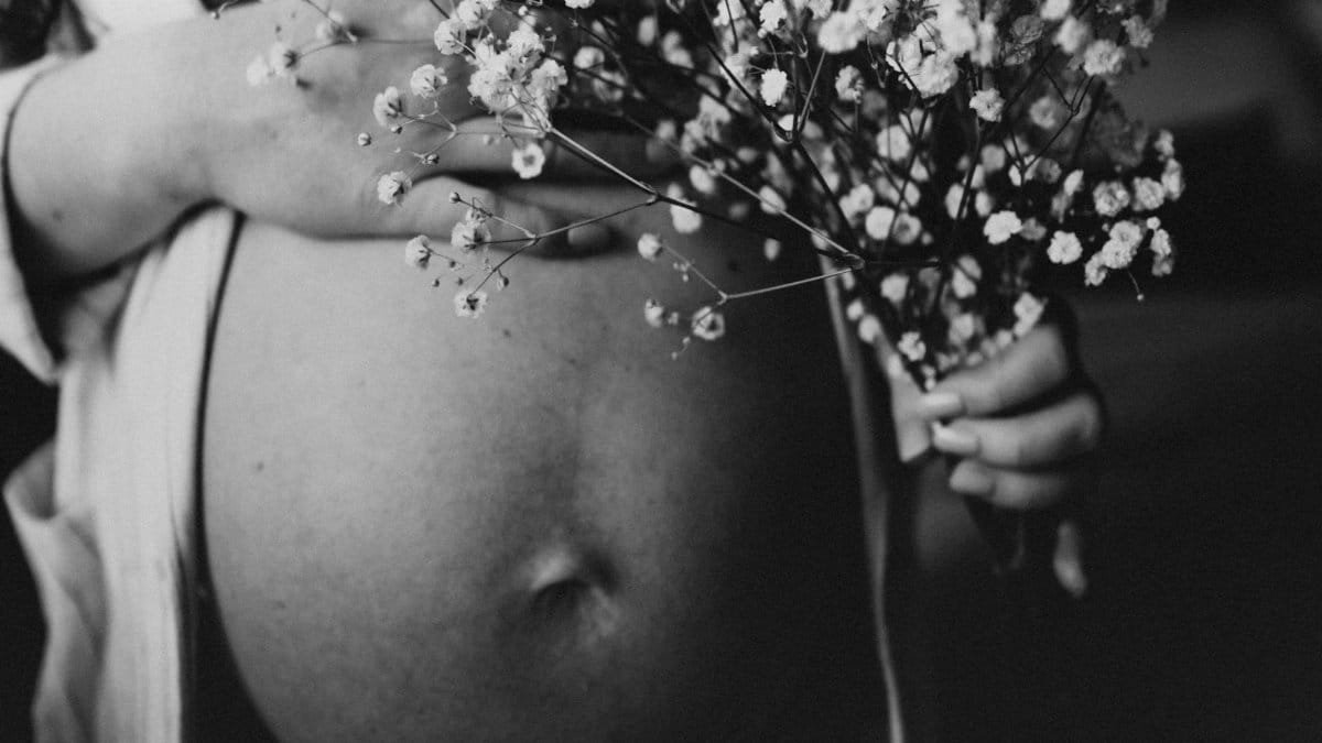 Artistic black and white photo of a pregnant woman holding flowers against her belly.