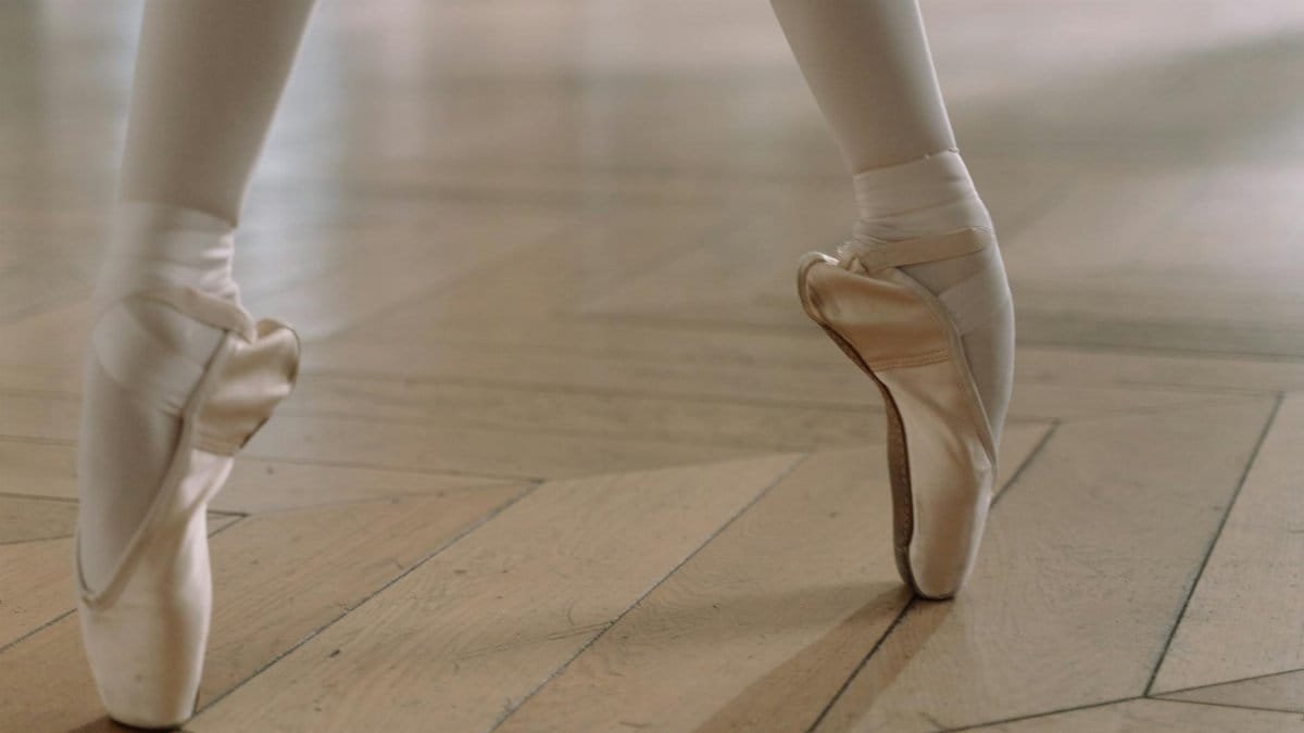 Close-up of a ballerina's feet in pointe shoes, showcasing grace and balance on a wooden floor.