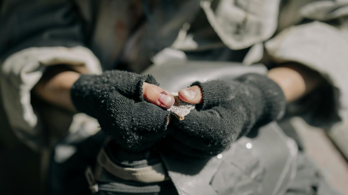 Rugged hands with fingerless gloves holding a fragment, depicting survival and resilience.