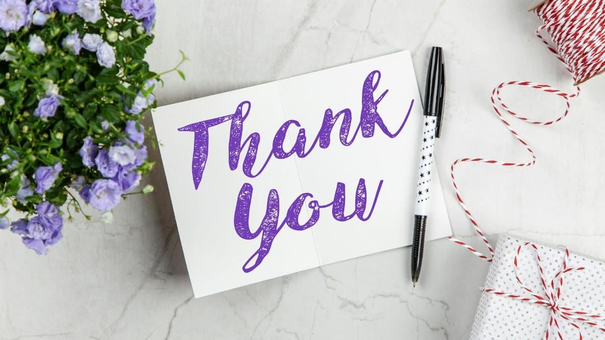 A stylish thank you card paired with purple flowers, a gift box, and pen on a marble surface.