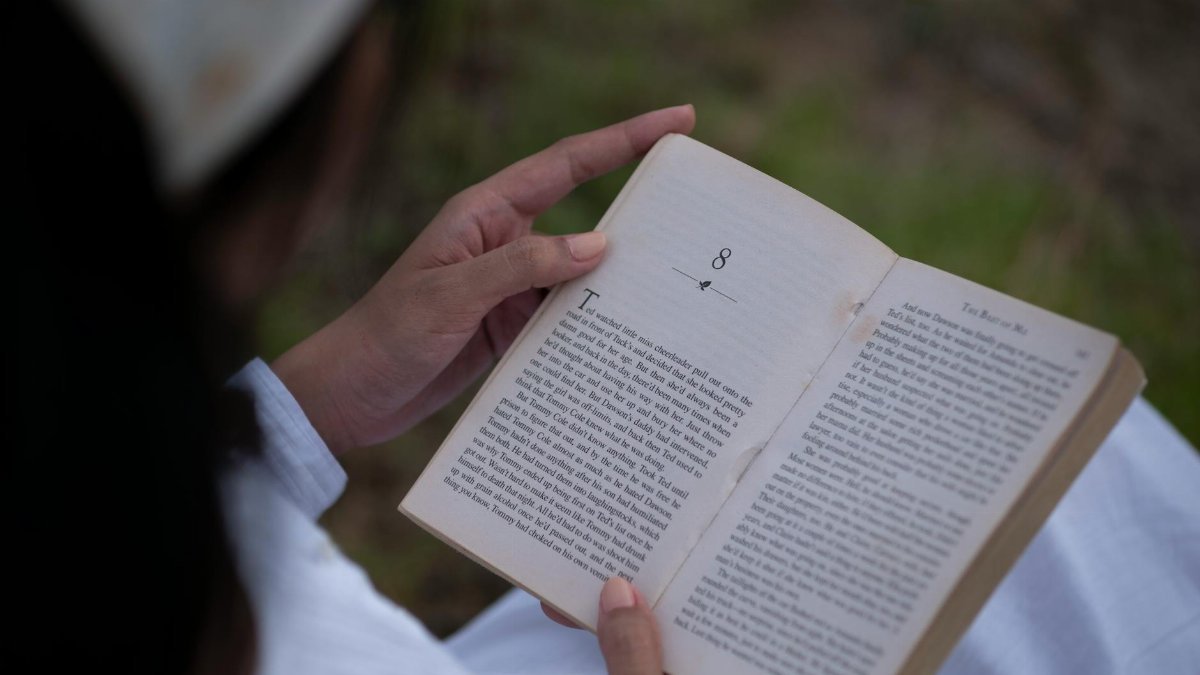 Person reading a book outdoors, enjoying a moment of tranquility and knowledge.