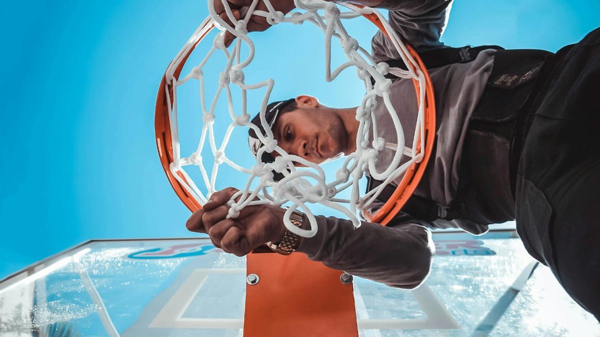 Close-up of a man adjusting a basketball hoop against a clear blue sky background.