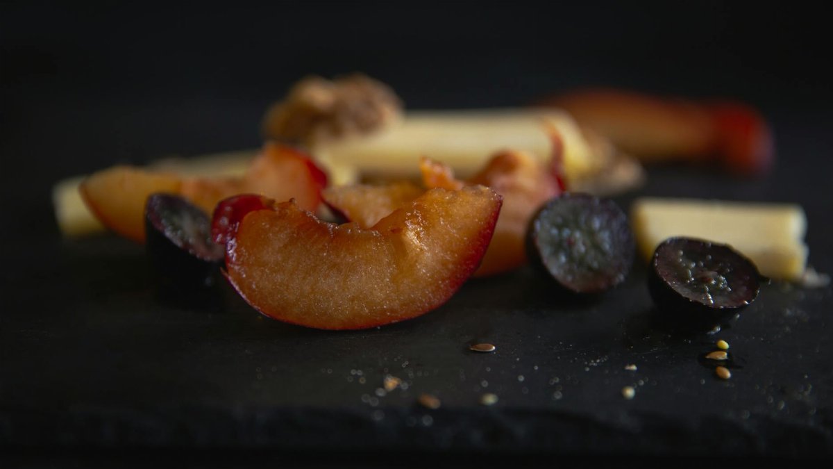 Close-up of fresh plum slices on black slate with cheese and seeds. Perfect for food blogs and culinary visuals.