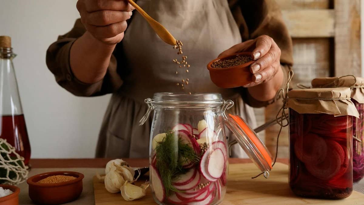 Close-up of hands preparing homemade pickles with spices in a rustic kitchen setting.