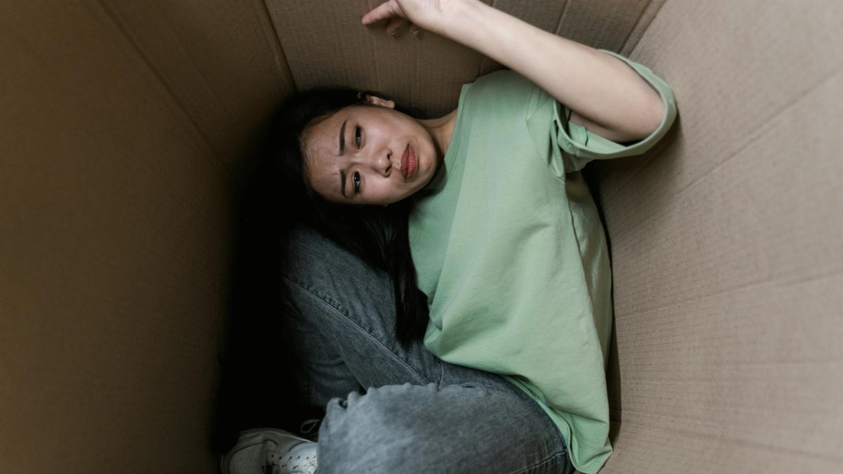 Woman enclosed in a cardboard box, showing signs of stress and fear.