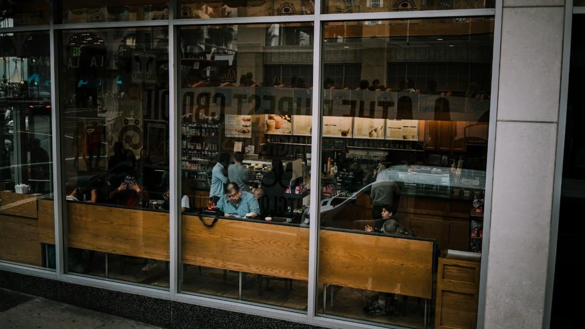 View through window of bustling cafe with customers inside, reflecting city life.