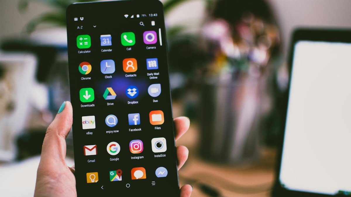 A close-up image of a person's hand holding a smartphone displaying various popular apps.