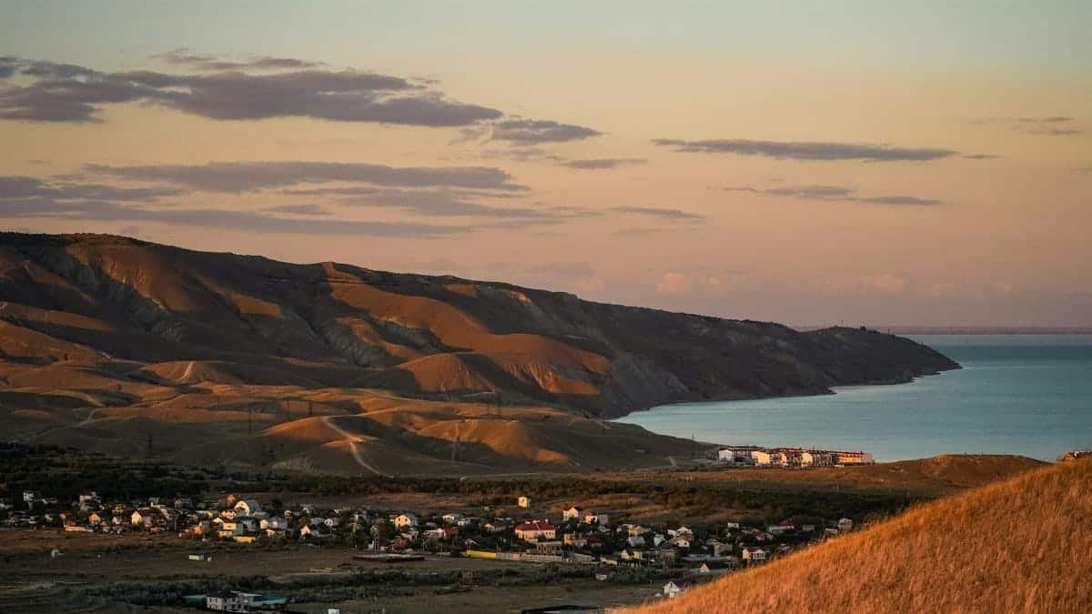 Capture of a tranquil coastal village in Crimea with rolling hills and a serene sea at sunset.