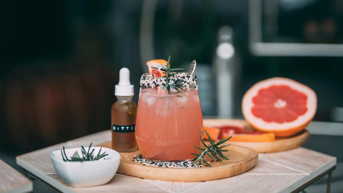 A chilled grapefruit cocktail garnished with fresh rosemary and sesame seeds.