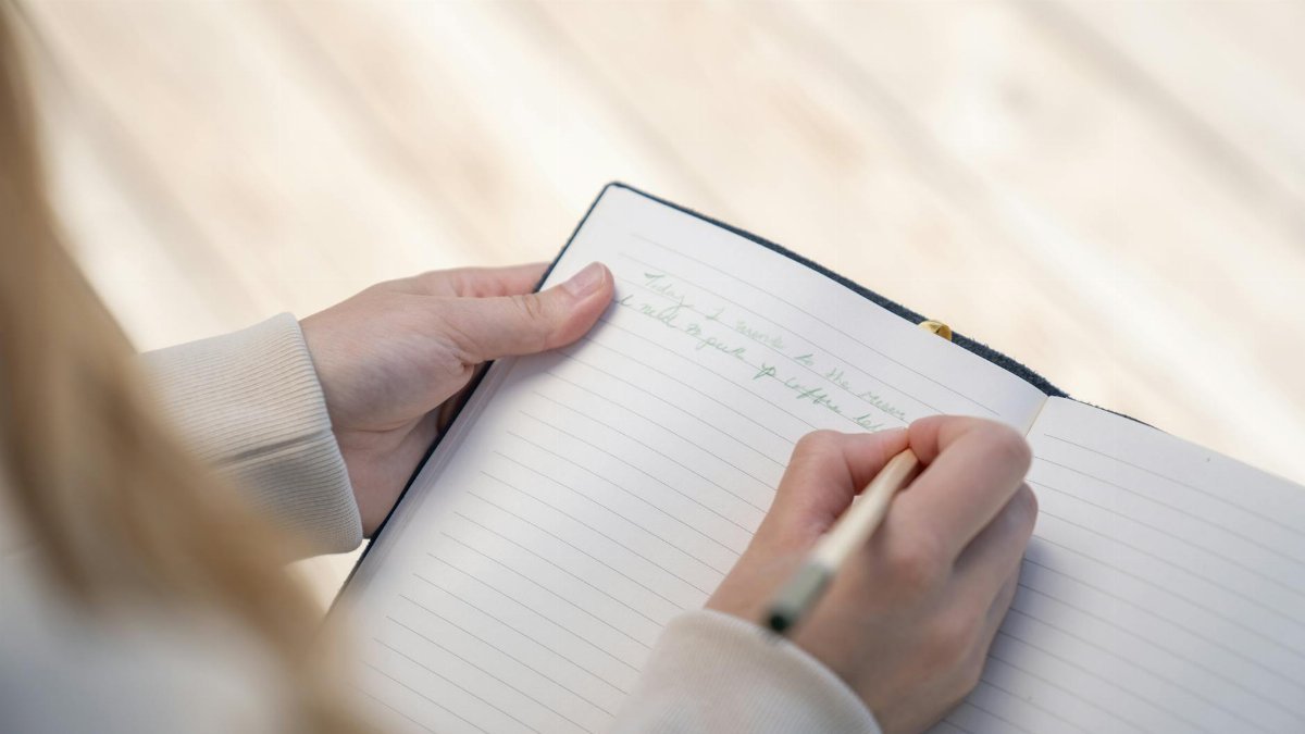 A person writing in a notebook with a pen, capturing a close-up view of hands.
