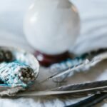 A spiritual arrangement featuring a crystal ball, sage bundle, and feathers, ideal for mystical themes.