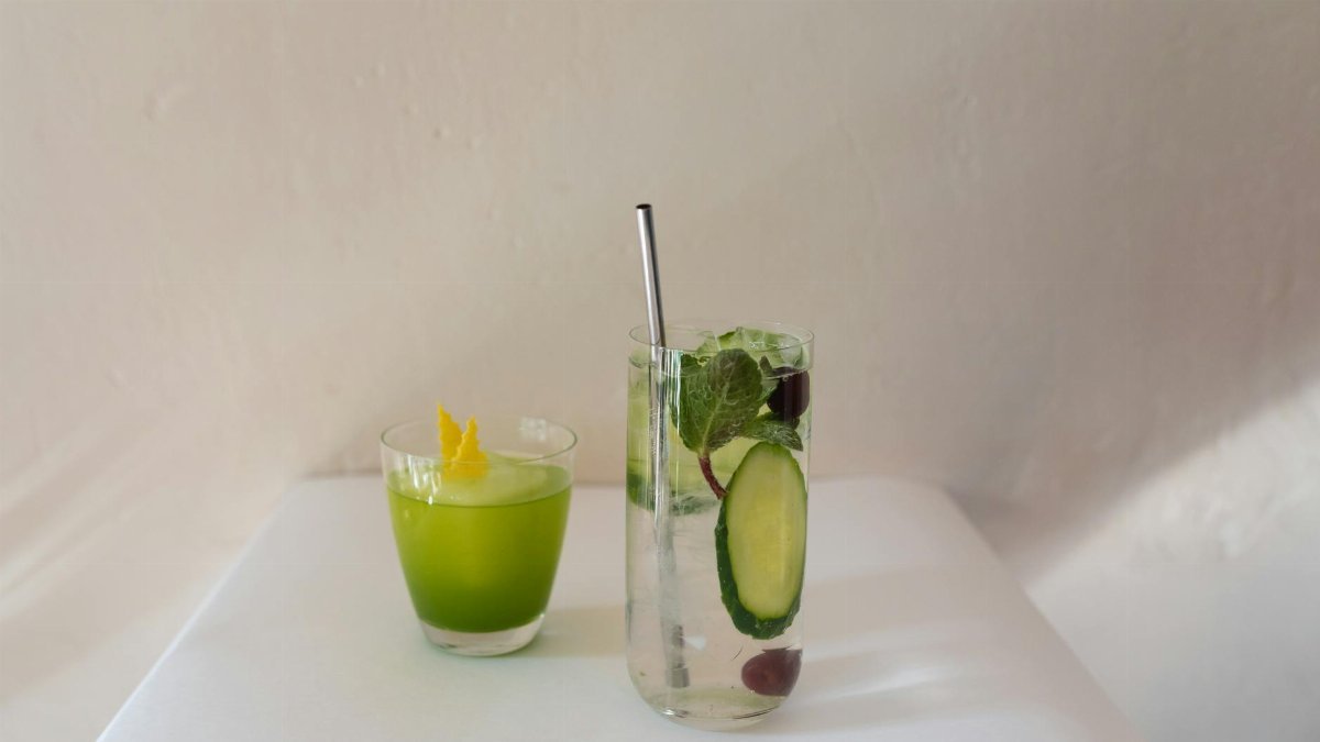 Two refreshing drinks with mint and cucumber garnish on a white table, perfect for a summer setting.
