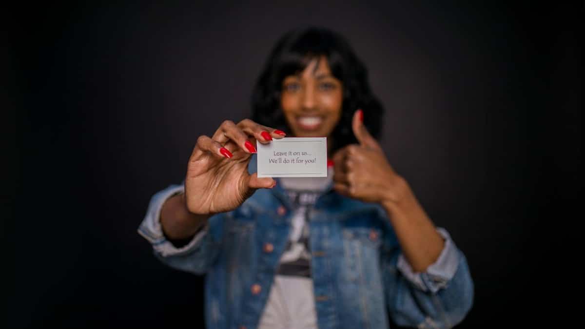 Smiling woman holding a business card with a message in focus, thumbs up sign.