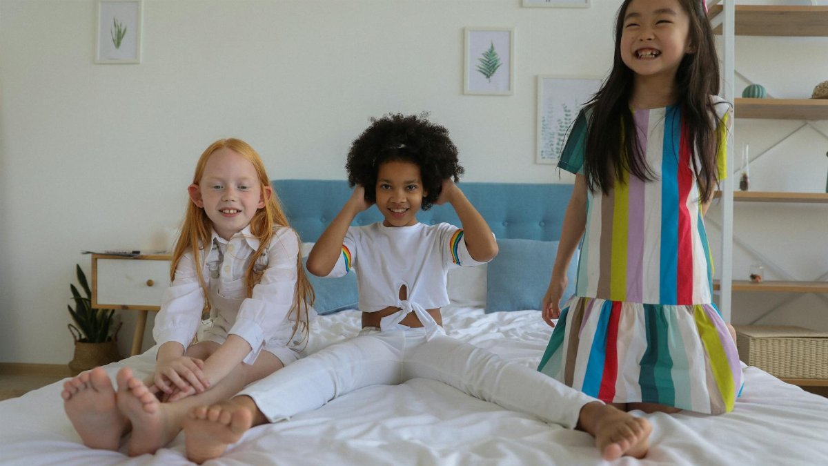 Three diverse children enjoying playtime on a bed in a bright and cozy bedroom setting.