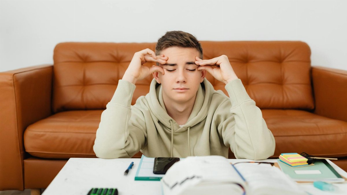 Young man experiencing stress while studying at home, wearing a hoodie.