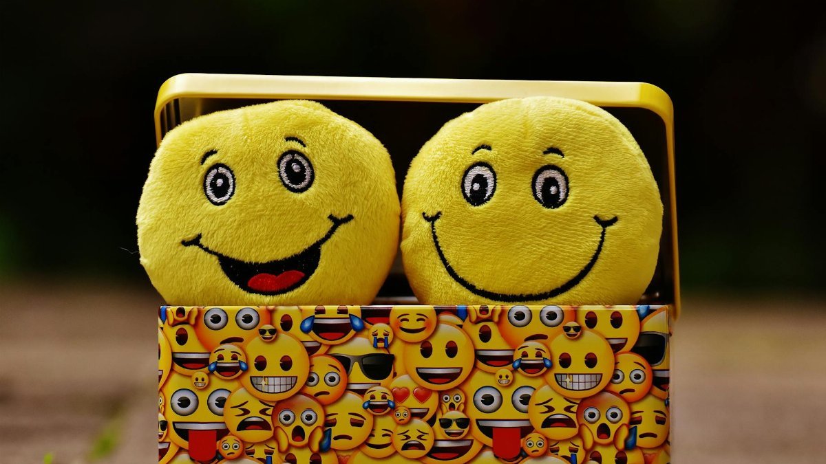 Two yellow smiley plush toys in an emoji-themed box, expressing fun and happiness.