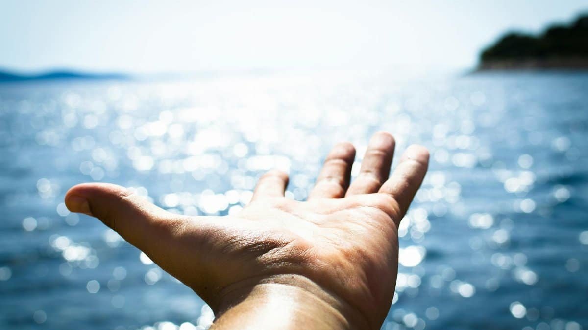 A hand reaching towards the sparkling sea, symbolizing freedom and hope.