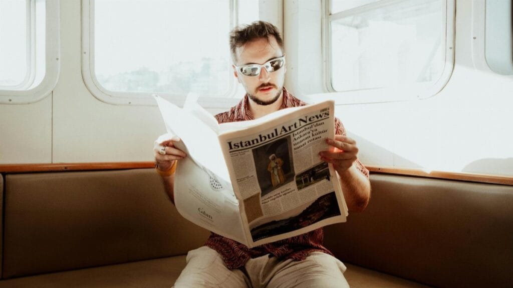 Adult man reading 'Istanbul Art News' on a sunny ferry ride in İstanbul, Türkiye.