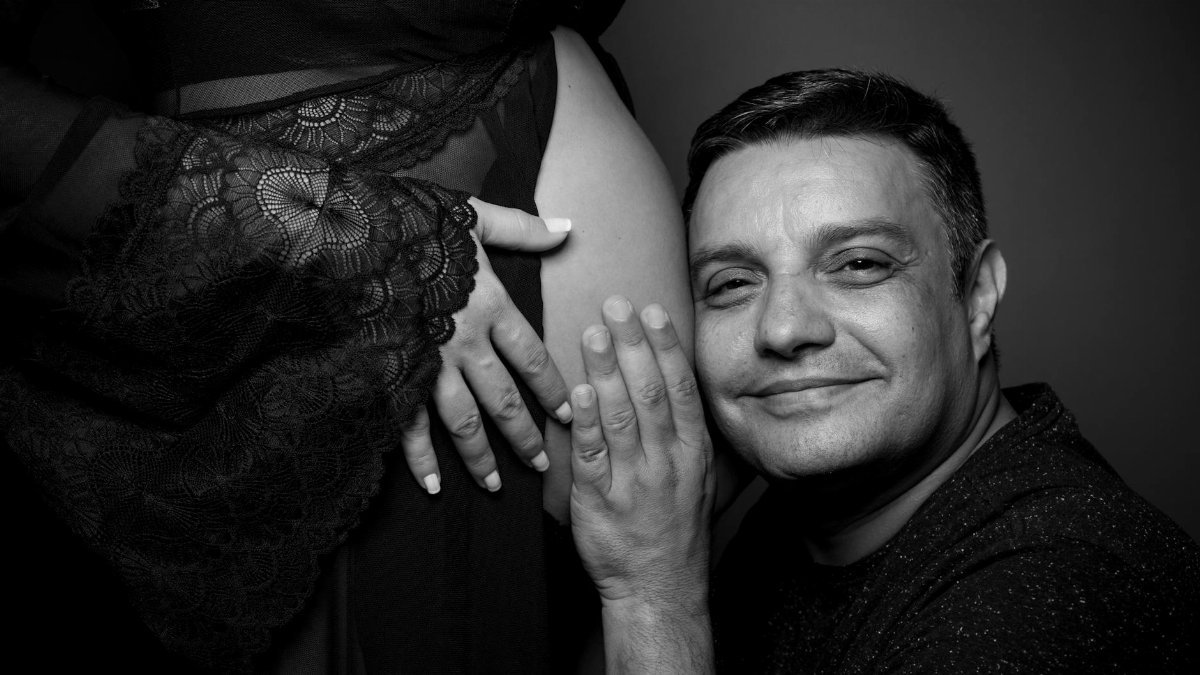 A loving expectant father embraces his partner's baby bump in a monochrome portrait.