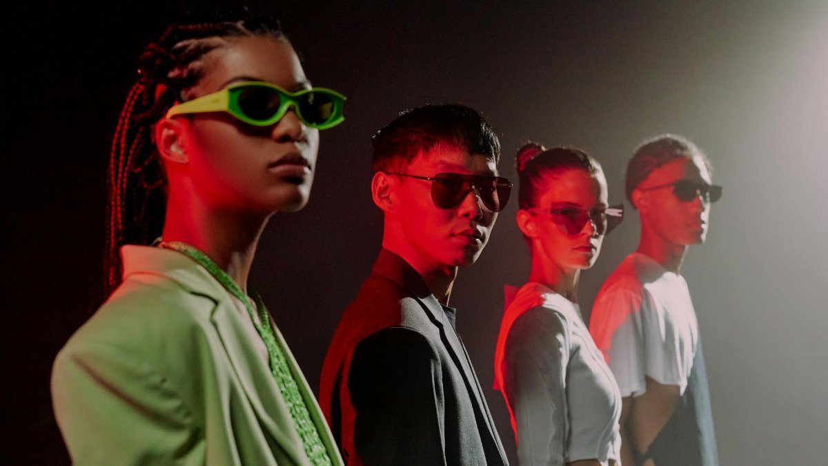 A diverse group of adults wearing sunglasses under dramatic red lighting, showcasing modern fashion and eyewear.