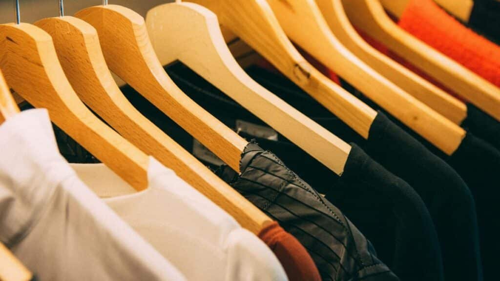 A close-up view of a row of clothes on wooden hangers, showcasing various fabrics and colors in a wardrobe setting.