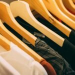A close-up view of a row of clothes on wooden hangers, showcasing various fabrics and colors in a wardrobe setting.