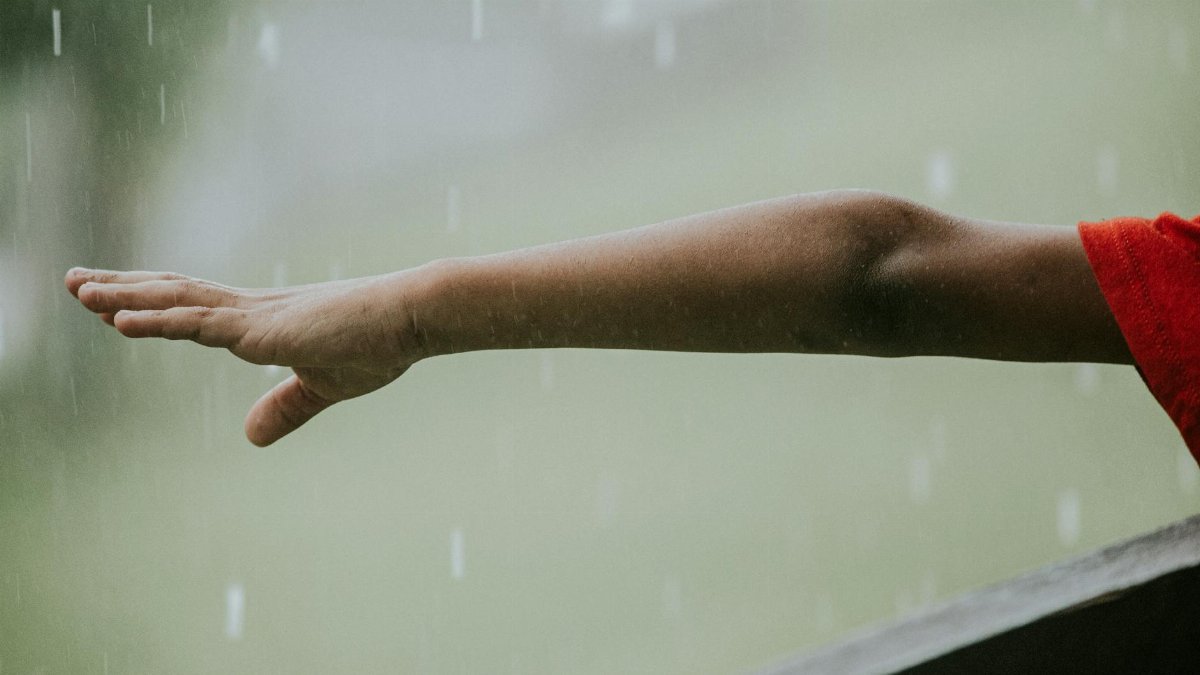 Child's arm extended outside, feeling the rain. Captures innocence and weather contrast.
