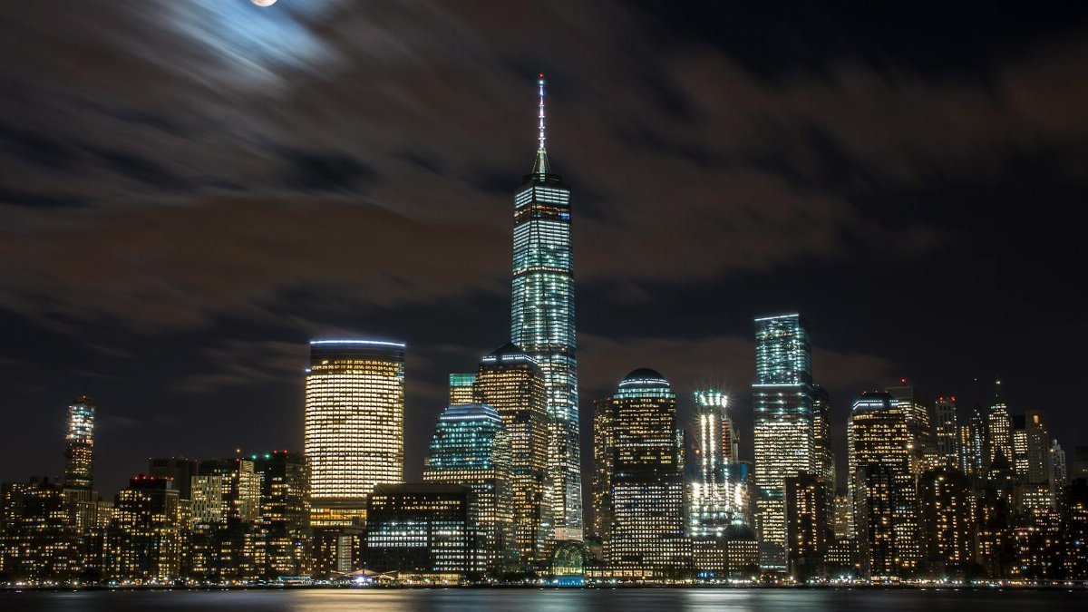 Captivating night view of New York City skyline under a full moon and reflective waters.
