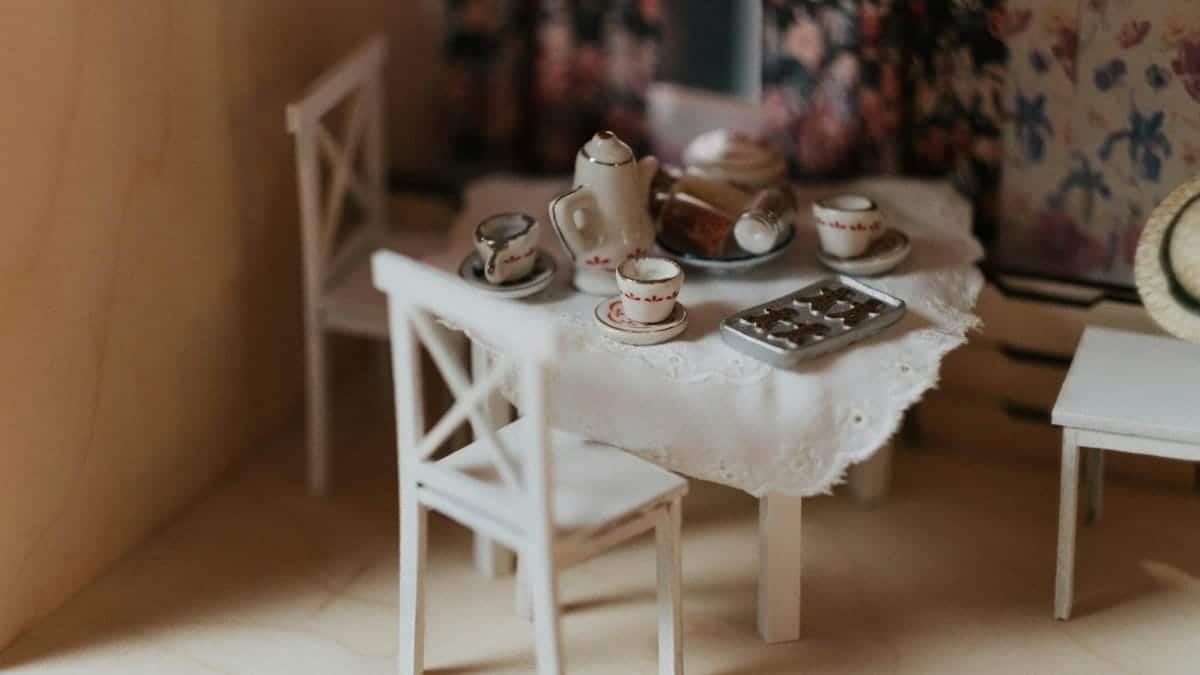 Charming miniature dollhouse dining room with an elegant tea set on a laced tablecloth.