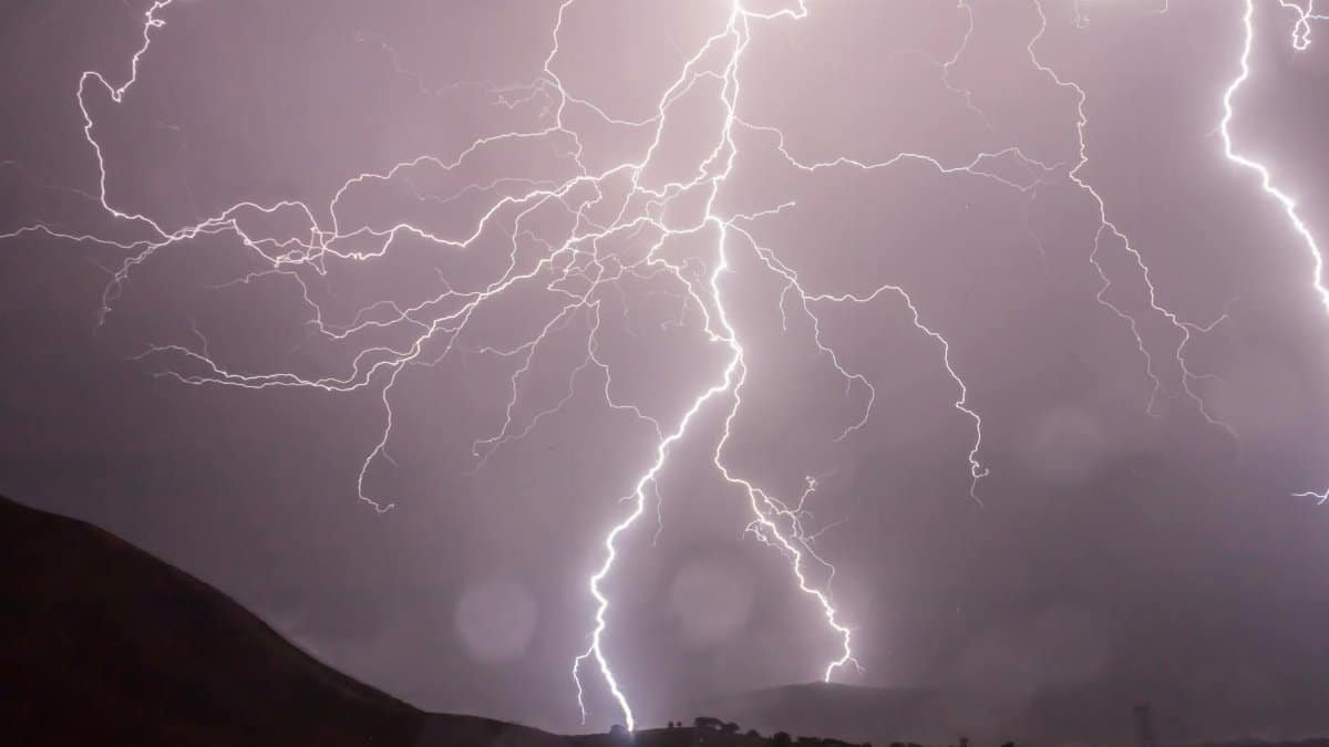 Captivating lightning bolts illuminate the night sky over dark hills in a dramatic weather display.