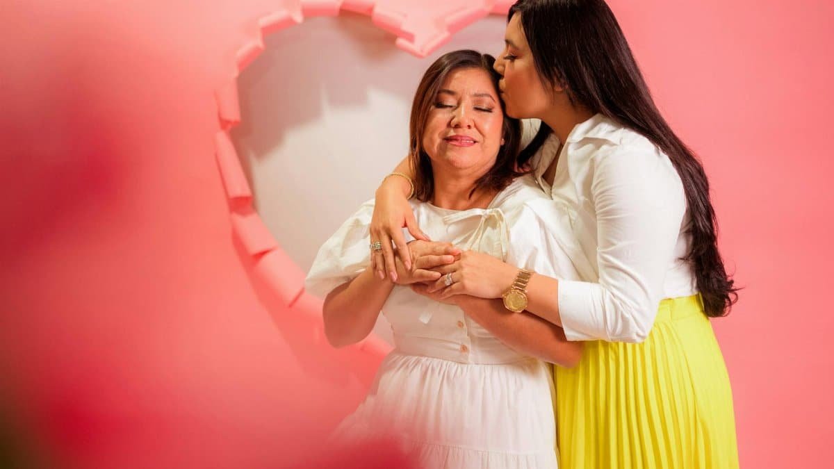 A tender moment of mother and daughter in front of a paper heart background.