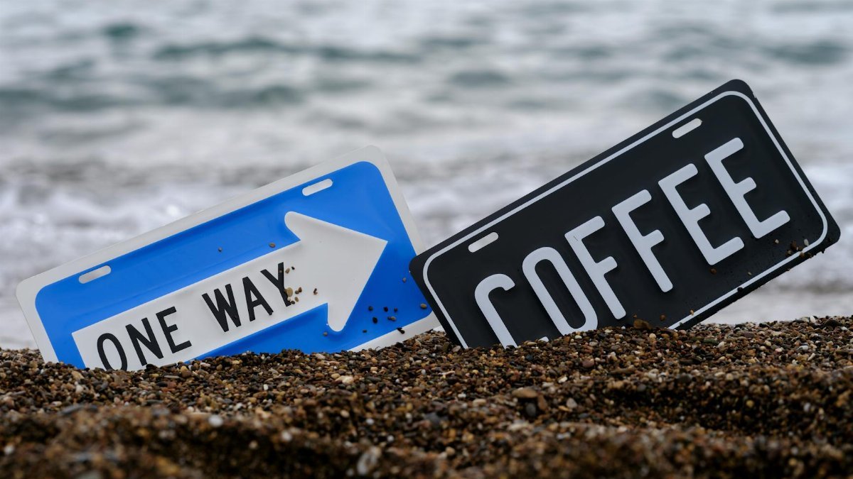 A beach scene with 'Coffee' and 'One Way' signs in the sand near the ocean.