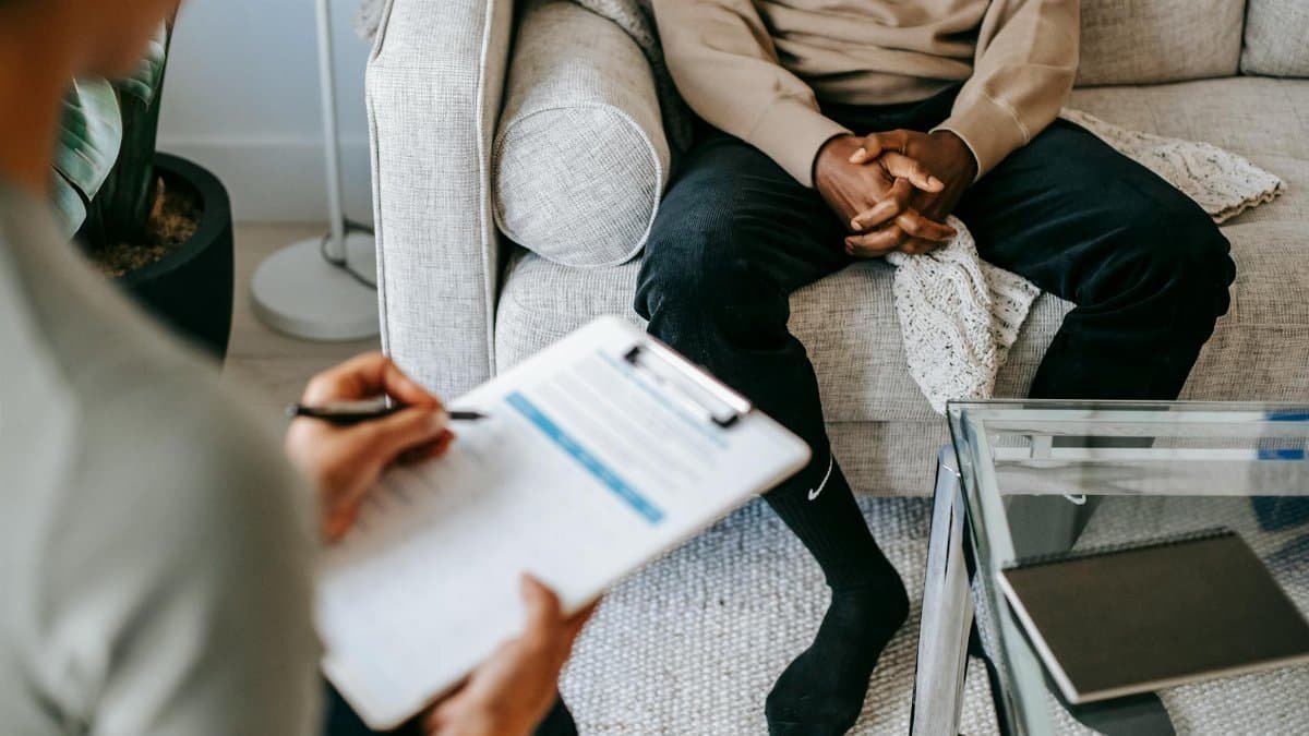 Therapist takes notes as client sits on a sofa during a psychotherapy session.