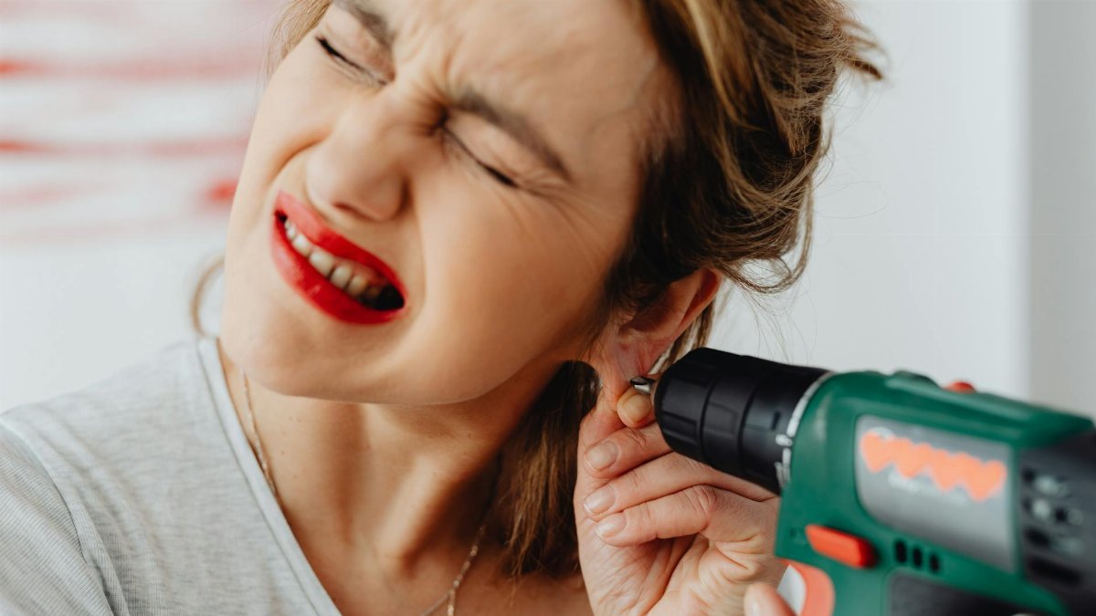 Woman's humorous expression as she uses a drill near her earring.