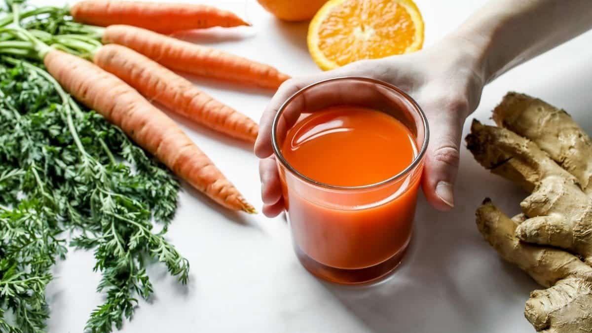Vibrant carrot and ginger juice surrounded by fresh ingredients on a clean surface.