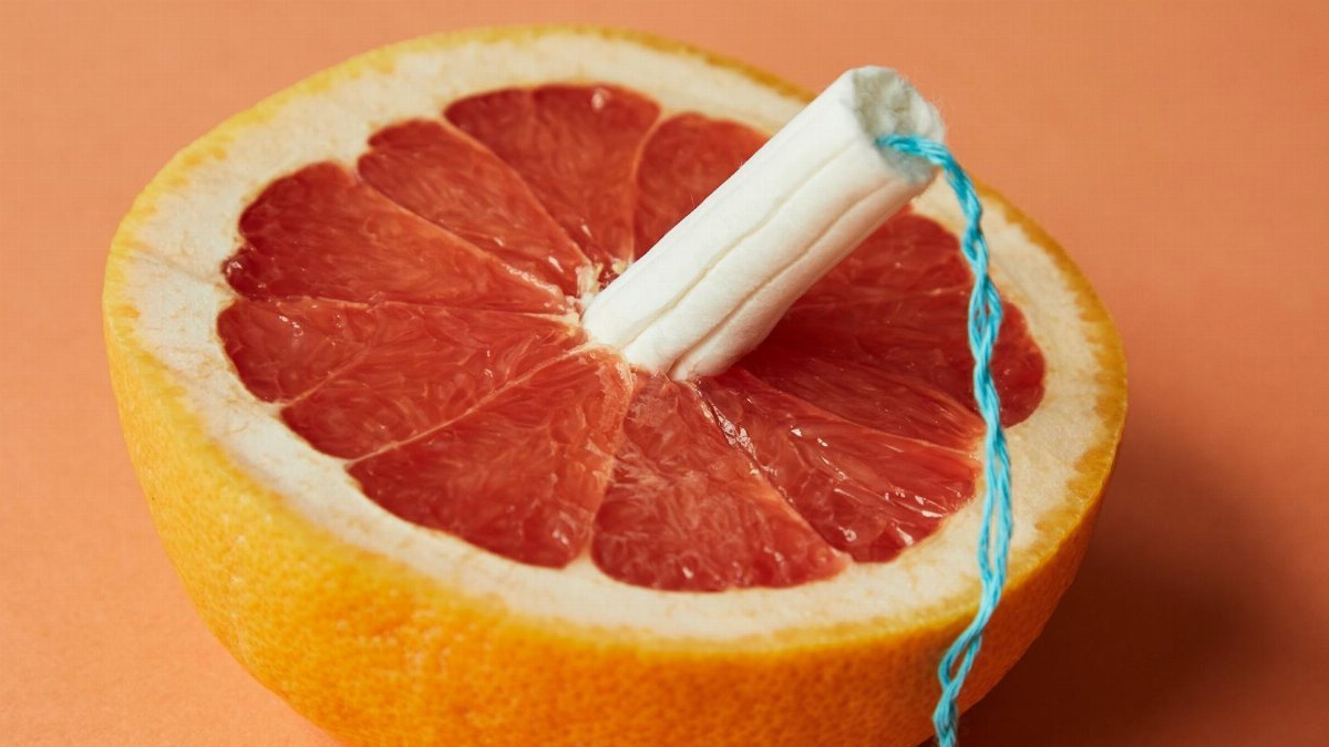 From above of half of sliced ripe grapefruit with tampon in center showing use of feminine product during menstruation