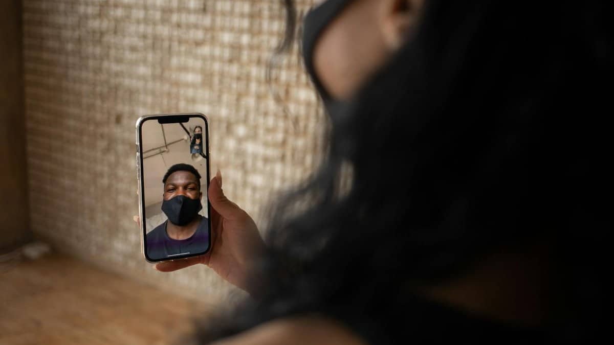 Back view of crop anonymous female talking to ethnic male beloved in fabric mask during video call on cellphone