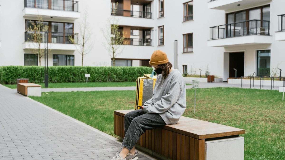 Tired food delivery worker in urban area sitting with backpack during the day.