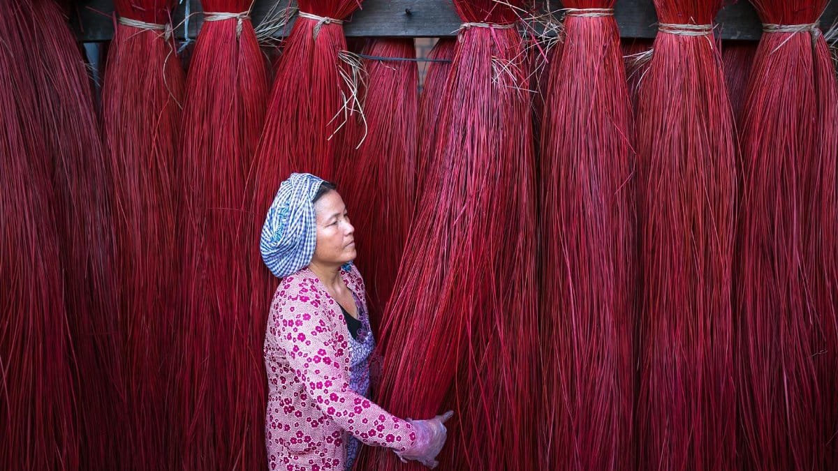A woman in traditional attire handles vibrant red fibers, showcasing cultural craftsmanship.